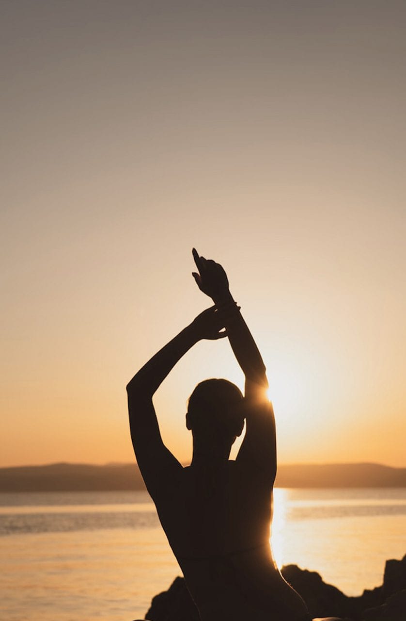 A person in a yoga pose at golden hour by the sea at sunset